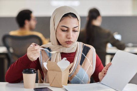 Foto de Retrato de una joven empresaria musulmana comiendo comida para llevar en el lugar de trabajo de la oficina y leyendo documentos, espacio para copiar - Imagen libre de derechos