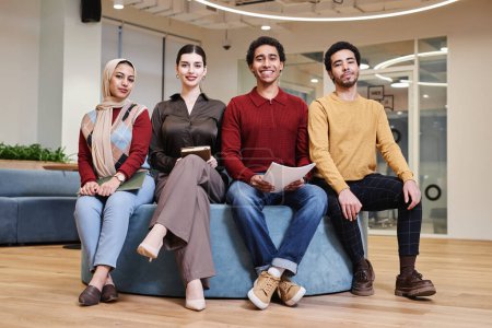 Foto de Retrato de larga duración del joven equipo de negocios de Oriente Medio posando juntos en una oficina moderna mirando alegremente a la cámara - Imagen libre de derechos
