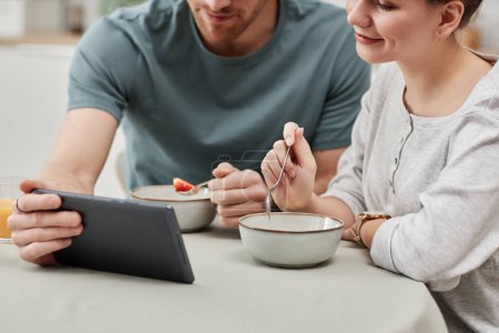 Foto de Primer plano de pareja joven usando tableta digital mientras disfruta del desayuno en la cocina, espacio para copiar - Imagen libre de derechos