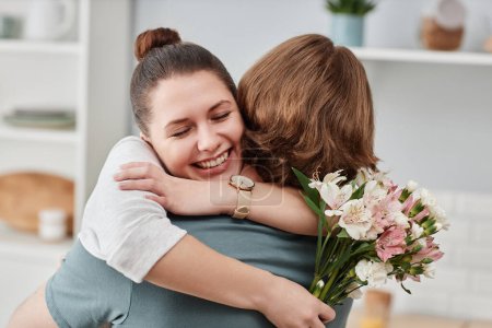 Téléchargez les photos : Gros plan de jeune homme donnant bouquet de fleurs à la femme et embrassant dans la cuisine - en image libre de droit