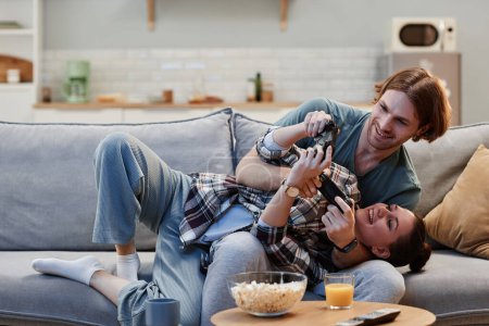 Foto de Retrato de pareja joven juguetona jugando videojuegos en el sofá en casa y sosteniendo controladores, espacio para copiar - Imagen libre de derechos