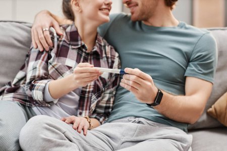 Téléchargez les photos : Gros plan d'un jeune couple heureux tenant un test de grossesse et embrassant à la maison - en image libre de droit