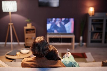 Téléchargez les photos : Vue arrière du couple regardant la télévision ensemble assis sur le canapé à la maison le soir, espace de copie - en image libre de droit
