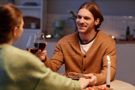 Photo for Portrait of smiling young man drinking wine with wife and enjoying romantic dinner at home - Royalty Free Image