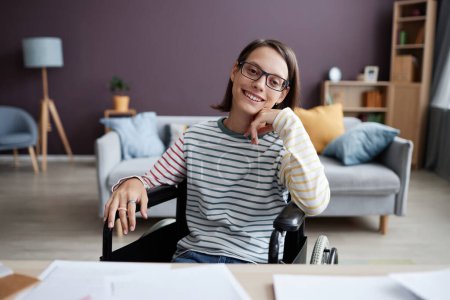 Foto de Retrato de vista frontal de una adolescente sonriente con discapacidad mirando a la cámara en el escritorio en el interior del hogar, espacio de copia - Imagen libre de derechos
