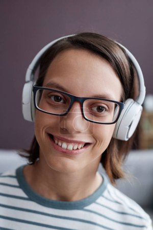 Foto de Retrato vertical de primer plano de una adolescente sonriente con discapacidad que usa auriculares en casa y mira la cámara - Imagen libre de derechos