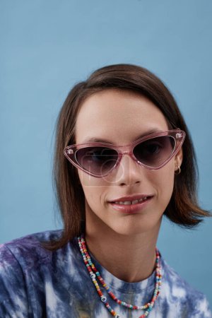 Foto de Retrato de moda de una adolescente con parálisis cerebral posando con confianza usando gafas de sol contra el azul - Imagen libre de derechos