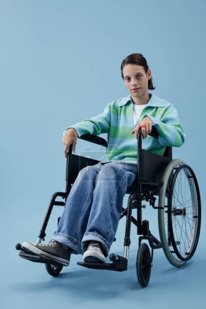 Foto de Retrato vertical de larga duración de adolescente con discapacidad mirando a la cámara en el estudio sobre fondo azul - Imagen libre de derechos