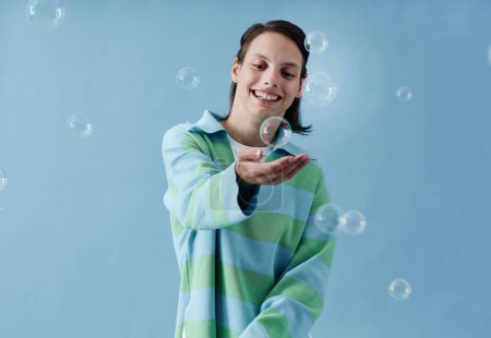 Photo for Waist up portrait of teenage girl with disability looking at camera smiling happily with bubbles against blue - Royalty Free Image