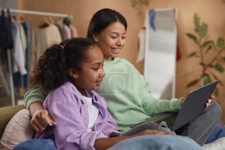 Photo for Side view portrait of young black mother and daughter using laptop together in cozy room - Royalty Free Image