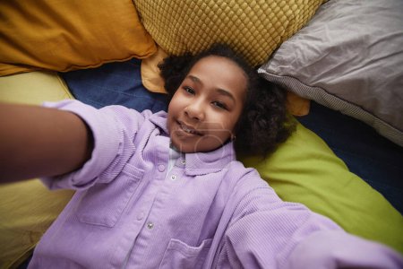 Photo for Top view POV of young black girl taking selfie photo lying in bed and looking at camera - Royalty Free Image