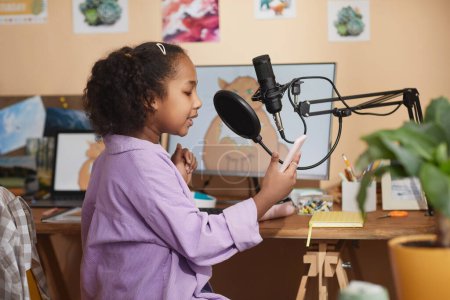 Foto de Retrato de vista lateral de una joven negra hablando con un micrófono en el video blog de grabación en casa o podcast - Imagen libre de derechos