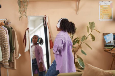 Foto de Vista posterior de la joven chica negra bailando por el espejo con auriculares en casa, espacio de copia - Imagen libre de derechos