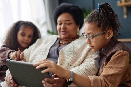 Foto de Retrato de vista lateral de adolescente niña negra enseñando abuela usando tableta digital en casa - Imagen libre de derechos