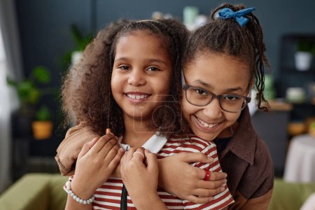 Foto de Retrato de dos chicas afroamericanas abrazando y mirando a la cámara en casa - Imagen libre de derechos