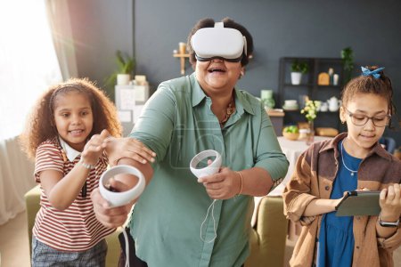 Photo for Waist up portrait of modern senior Black woman playing VR game with little girls in sunlight and having fun - Royalty Free Image