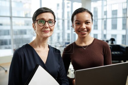 Photo for Front view portrait of two modern businesswomen smiling at camera in luxury office interior - Royalty Free Image
