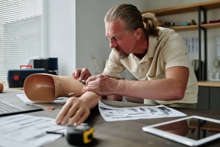 Téléchargez les photos : Side view portrait of senior man building arm prosthetics in workshop and installing wiring, copy space - en image libre de droit