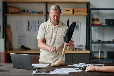 Téléchargez les photos : Portrait à la taille de prothèses de jambes de bâtiment senior homme dans l'atelier mesurant soigneusement les pièces, l'espace de copie - en image libre de droit