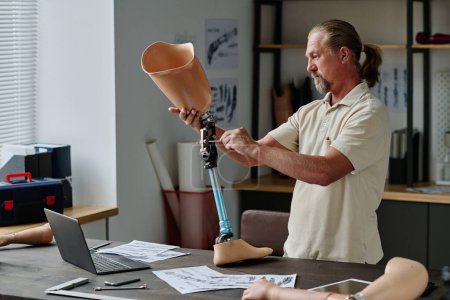 Téléchargez les photos : Portrait latéral d'un artisan chevelu construisant des prothèses de jambes en atelier et vissant des joints, espace de copie - en image libre de droit