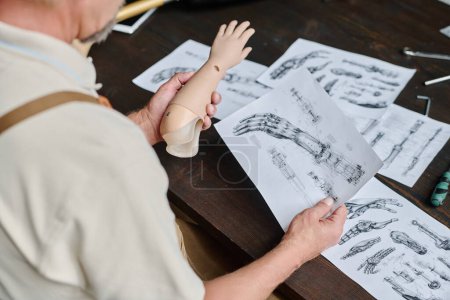 Téléchargez les photos : Gros plan de l'artisan regardant les plans détaillés et les plans de prothèses dans l'atelier, l'espace de copie - en image libre de droit