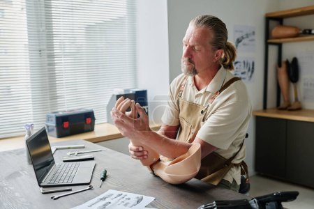 Téléchargez les photos : Portrait d'un artisan barbu inspectant des prothèses de bras dans un atelier avec ordinateur portable sur la table, espace de copie - en image libre de droit