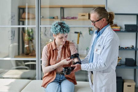 Téléchargez les photos : Portrait d'un médecin consultant une jeune femme et ajustant un bras prothétique dans une clinique d'orthologie - en image libre de droit