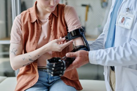 Closeup of doctor consulting young woman and fitting prosthetic arm in orthology clinic