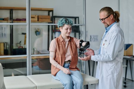 Portrait of smiling young woman with prosthetic arm consulting doctor in orthology clinic, copy space