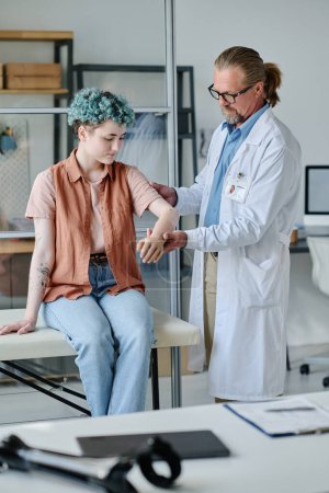 Vertical portrait of smiling young teenage girl with prosthetic arm consulting doctor in orthology clinic