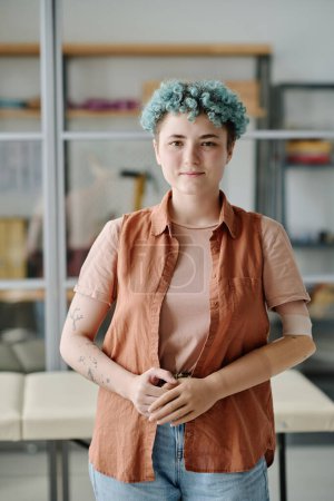 Téléchargez les photos : Portrait vertical de jeune femme avec un bras prothétique posant dans le bureau des médecins et souriant à la caméra - en image libre de droit