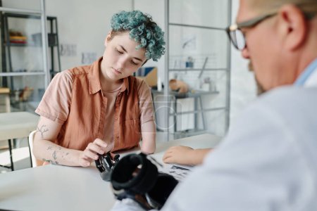 Téléchargez les photos : Portrait de jeune femme aux cheveux bleus consultant médecin en clinique d'orthologie lors de l'ajustement prothétique du bras - en image libre de droit