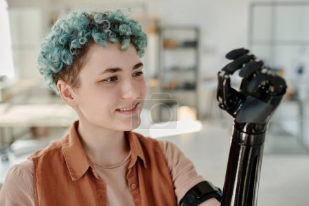 Téléchargez les photos : Portrait de jeune femme regardant le bras cyberprothétique et souriant - en image libre de droit