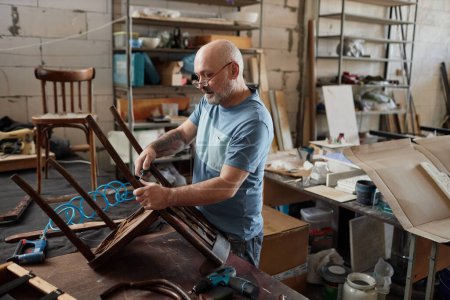 Téléchargez les photos : Portrait latéral d'un artisan chevronné restaurant une chaise vintage dans un atelier de meubles, espace de copie - en image libre de droit