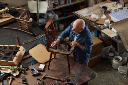 Téléchargez les photos : Portrait en grand angle d'un artisan chevronné fixant de vieux meubles dans un atelier, espace de copie - en image libre de droit