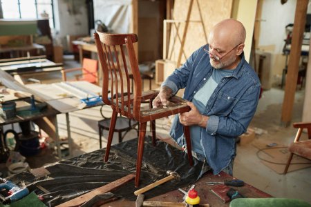 Foto de Retrato del artesano senior reparando muebles antiguos en taller de carpintería, espacio para copiar - Imagen libre de derechos
