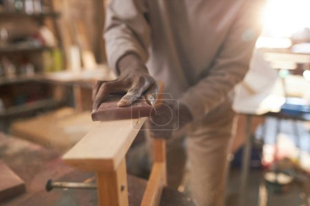 Foto de Primer plano del artesano negro cuidadosamente lijar muebles de madera en taller de carpintería rústica, espacio de copia - Imagen libre de derechos