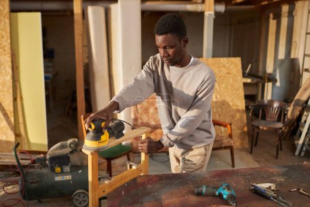Téléchargez les photos : Portrait à la taille d'un jeune homme noir concentré fabriquant des meubles en bois à la lumière du soleil, espace de copie - en image libre de droit