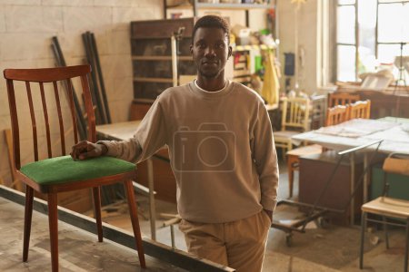 Téléchargez les photos : Portrait chaleureux de jeune homme afro-américain regardant la caméra dans l'atelier - en image libre de droit