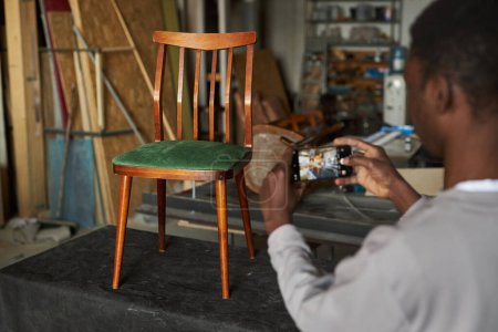 Closeup of man taking photo of vintage wooden chair for sale online, copy space