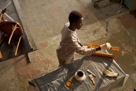 Téléchargez les photos : Vue du dessus du jeune homme noir faisant projet de restauration de meubles dans l'atelier, espace de copie - en image libre de droit