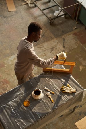 Téléchargez les photos : Jeune homme noir faisant bricolage projet de restauration de meubles en atelier - en image libre de droit