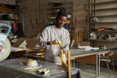 Foto de Retrato de cintura hacia arriba del joven afroamericano puliendo muebles de madera en el taller - Imagen libre de derechos