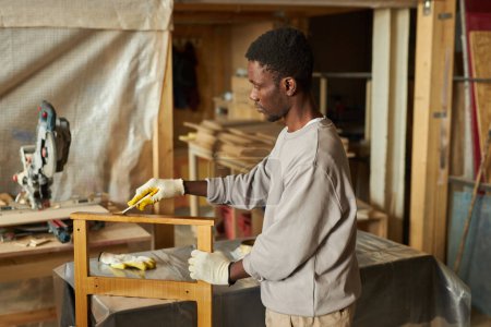Photo for Side view portrait of young African American man refinishing wooden furniture in workshop - Royalty Free Image