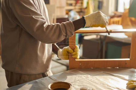 Side view closeup of African American man painting wooden furniture in workshop, copy space