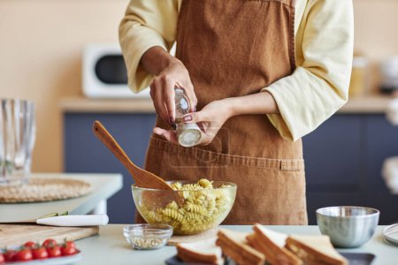 Foto de Primer plano de mujer negra irreconocible añadiendo especias a la pasta mientras se cocina en la cocina, espacio para copiar - Imagen libre de derechos