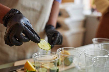 Photo for Close up of woman wearing glove adding lime slices to refreshing lemonade drinks in bar, copy space - Royalty Free Image