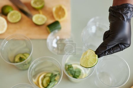 Photo for Top view closeup of young woman adding lime slices to drinks while making lemonade in bar, copy space - Royalty Free Image