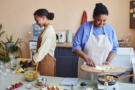 Foto de Retrato de dos jóvenes negras preparando comidas juntas cocinando en la cocina - Imagen libre de derechos