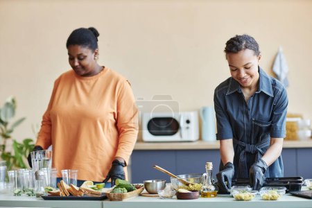 Photo for Portrait of two smiling African American women cooking together in kitchen and doing food prep at weekend - Royalty Free Image